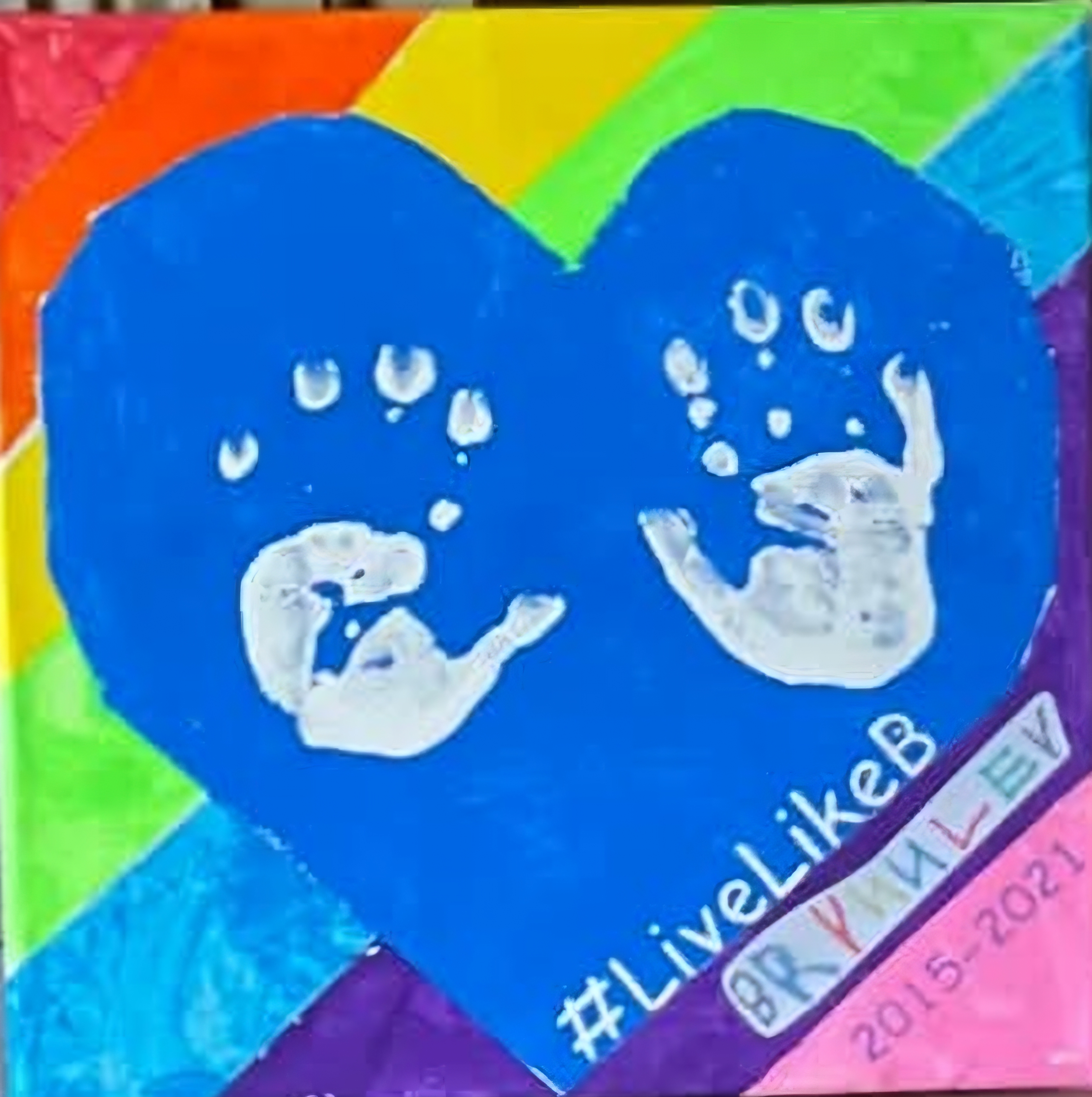 Rainbow painting with a blue heart, two white handprints, and Brynnley’s name